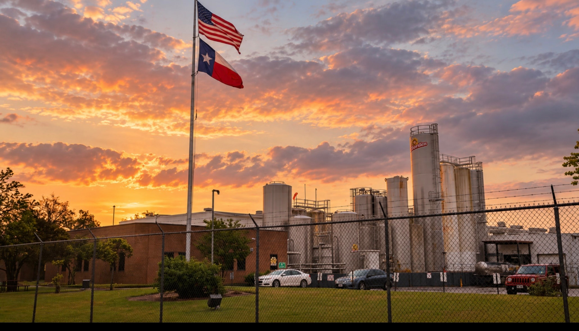 The Borden Dairy plant at sunset, with the American and Texas flags and the Borden silo tower